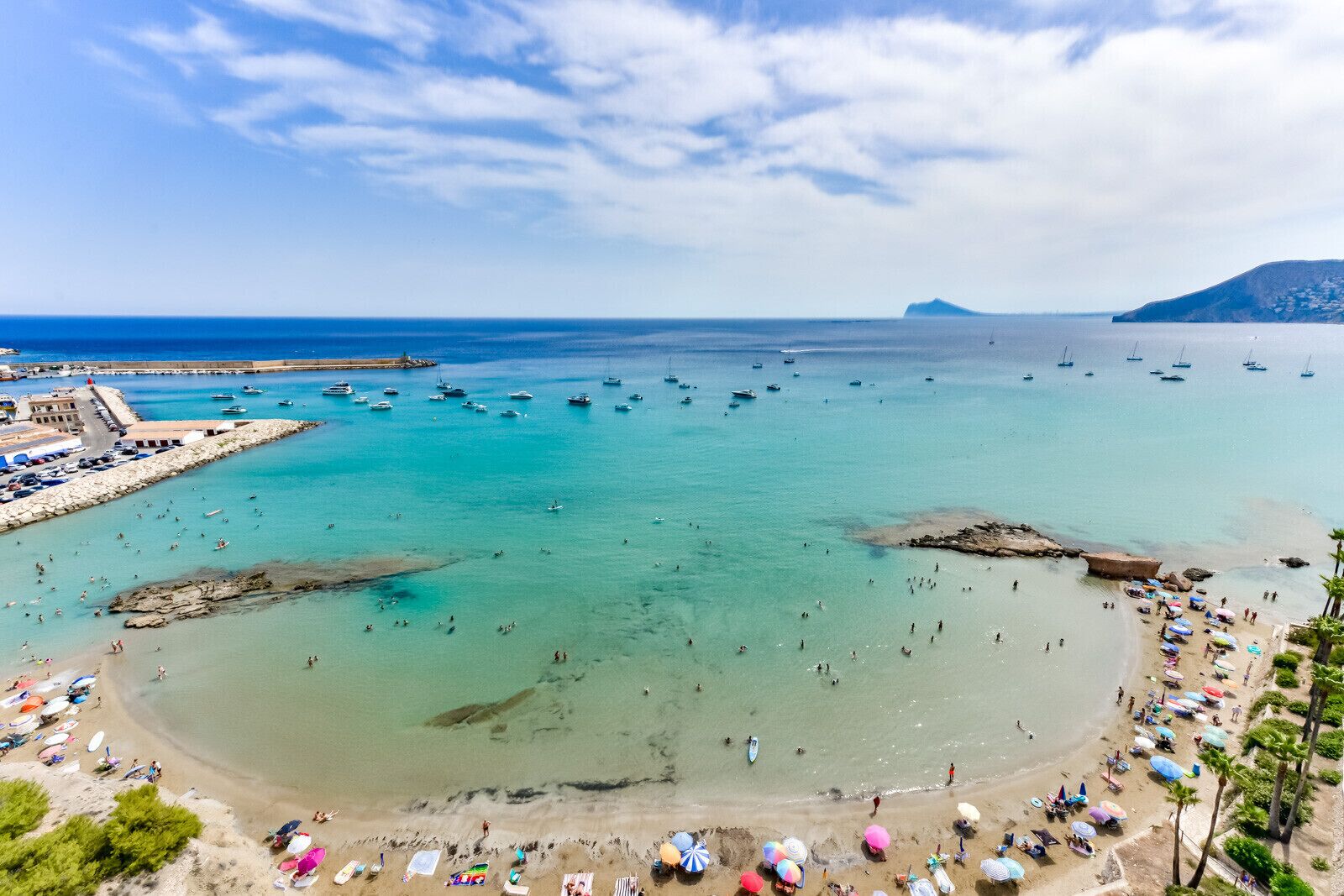 Una playa costera con aguas cristalinas, un rompeolas rocoso y un pequeño promontorio.