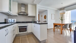 A modern kitchen with white cabinets, a stove, and a microwave. There is a dining area with a wooden table and chairs. - Apartment for rent in Calpe, BARLOVENTO (Calpe / Calp)
