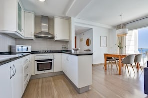 Eine moderne Küche mit weißen Schränken, einem Herd und einer Mikrowelle. Es gibt einen Essbereich mit einem Holztisch und Stühlen.