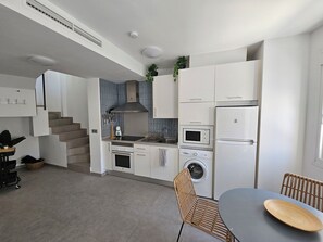 Eine kleine Küche mit weißen Schränken, einer Mikrowelle, einem Backofen, einer Waschmaschine und einem Essbereich mit Tisch und Stühlen.