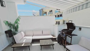 En tagterrasse med en hjørnesofa, et lille bord, en grill og en potteplante.