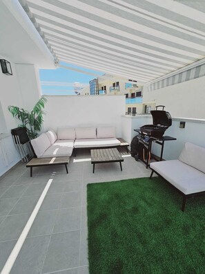 Eine Dachterrasse mit Ecksofa, einem kleinen Tisch, einem Grill und einem Blumentopf.