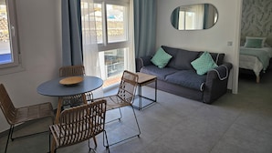 En moderne stue med sofa, stole, spisebord og et stort vindue med gardiner.