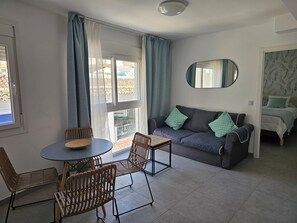Ein modernes Wohnzimmer mit einer Couch, Sesseln, einem Esstisch und einem großen Fenster mit Vorhängen.
