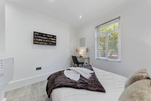 A modern bedroom with a bed, a desk, and a window with blinds. - The Modern Studio London (London)