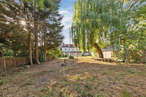 A backyard with a wooden fence, a tree, and a house in the background. - The Modern Studio London (London)