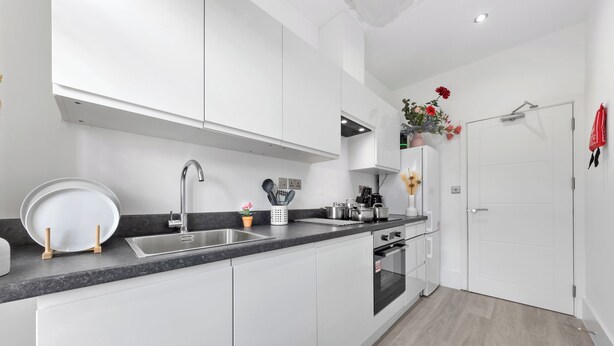Una cocina moderna con armarios blancos, un lavamanos de acero inoxidable y un horno empotrado.