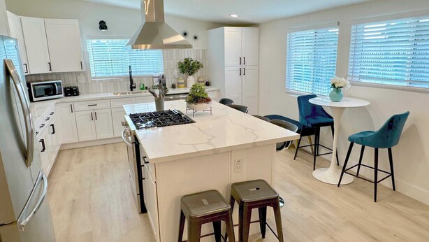 Une cuisine moderne avec des meubles blancs, un îlot central, une cuisinière et des tabourets de bar.