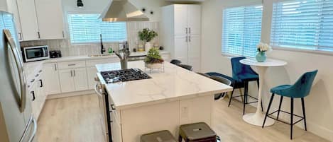 Una cocina moderna con armarios blancos, una isla central, estufa y taburetes de bar.