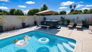 Une piscine avec un flotteur en forme de licorne, des chaises longues et un jacuzzi.