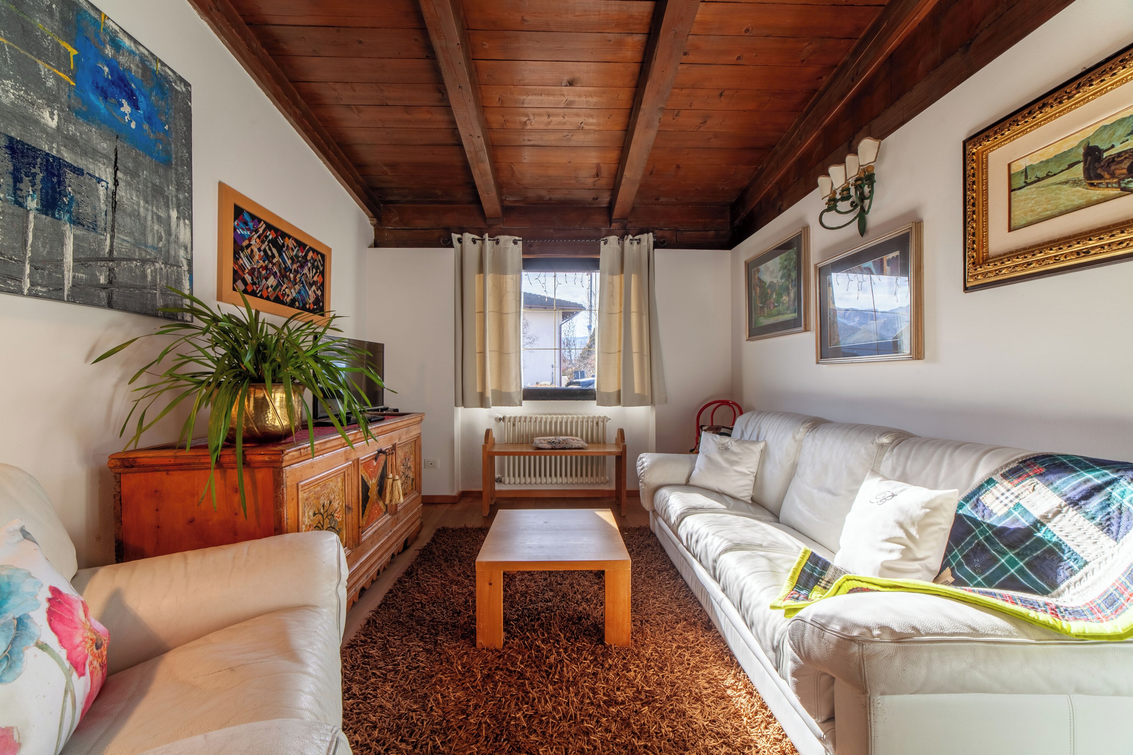 A living room with a wooden ceiling, a white sofa, a wooden coffee table, a radiator, and a potted plant.