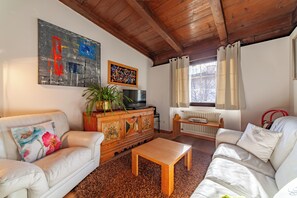 Un salon avec un plafond en bois, un canapé, une table basse, un téléviseur, un radiateur et une fenêtre avec des rideaux.