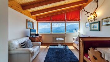 Una habitación acogedora con techo de madera, un sofá, una mesita, una cama y una ventana con vistas a la montaña.