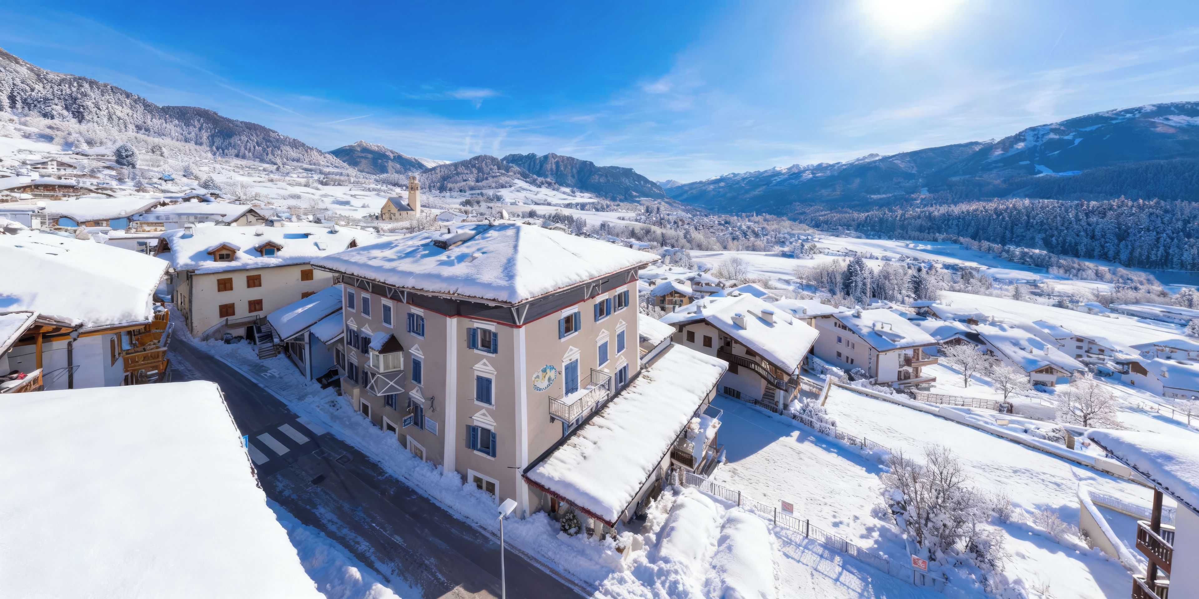 A snow-covered village with traditional buildings, a clear sky, and mountains in the background.