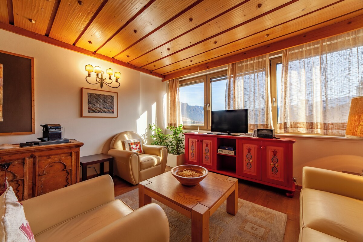 Un salon chaleureux avec un plafond en bois, un téléviseur, un meuble rouge et une grande fenêtre avec des rideaux.