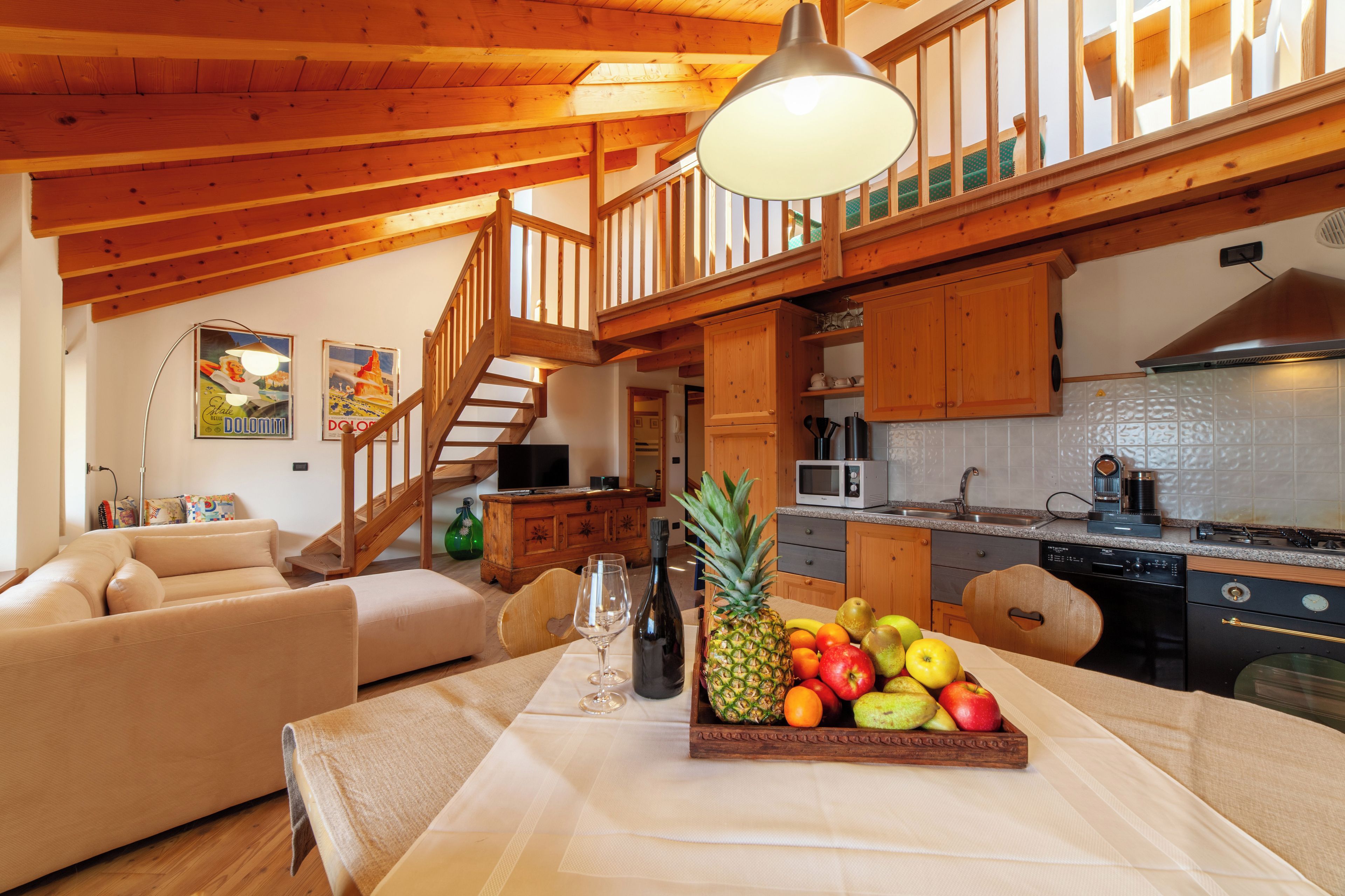 A wooden interior with a dining table, fruit bowl, and a staircase.