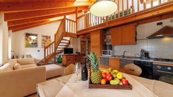 A wooden interior with a dining table, fruit bowl, and a staircase.