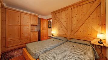 A bedroom with a large bed, wooden wardrobe, and a small table with a lamp.