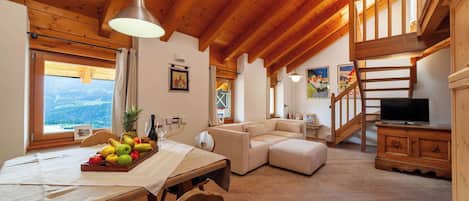 Un salón acogedor con techo de madera, un sofá, una mesa de comedor con fruta y un televisor.