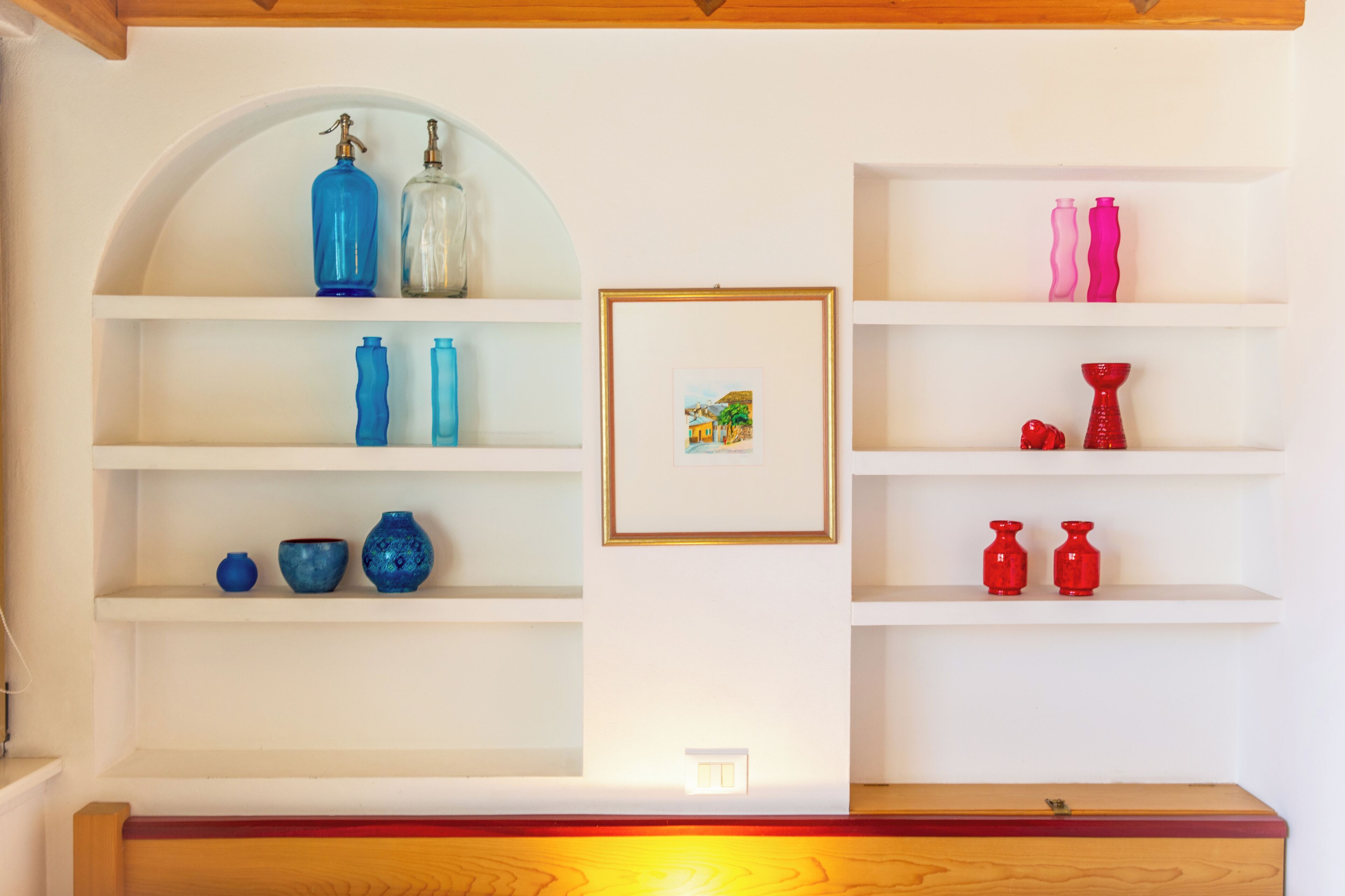 Une pièce aux murs blancs, avec des poutres en bois et des étagères ornées de différents vases et d’un tableau encadré.