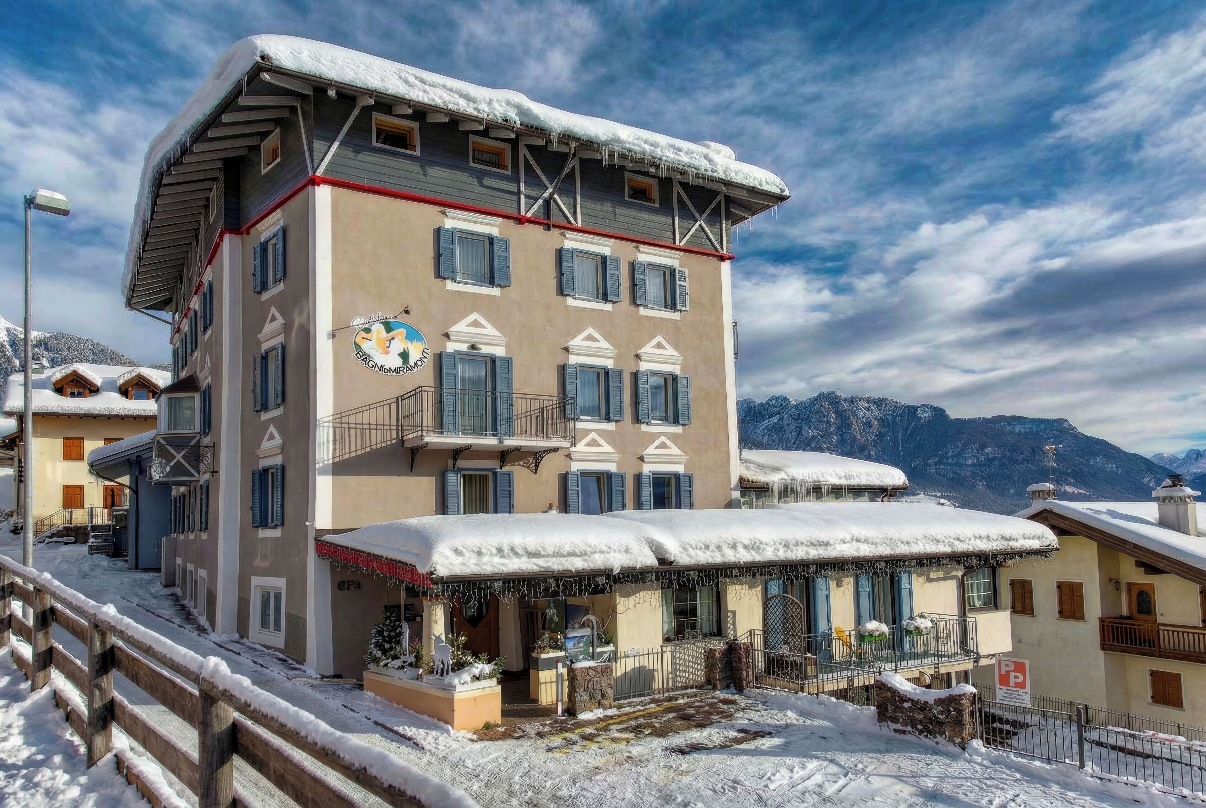Un hotel de varios pisos con techo nevado y balcones, frente a un paisaje montañoso.