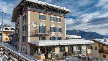 Un hotel de varios pisos con techo nevado y balcones, frente a un paisaje montañoso.