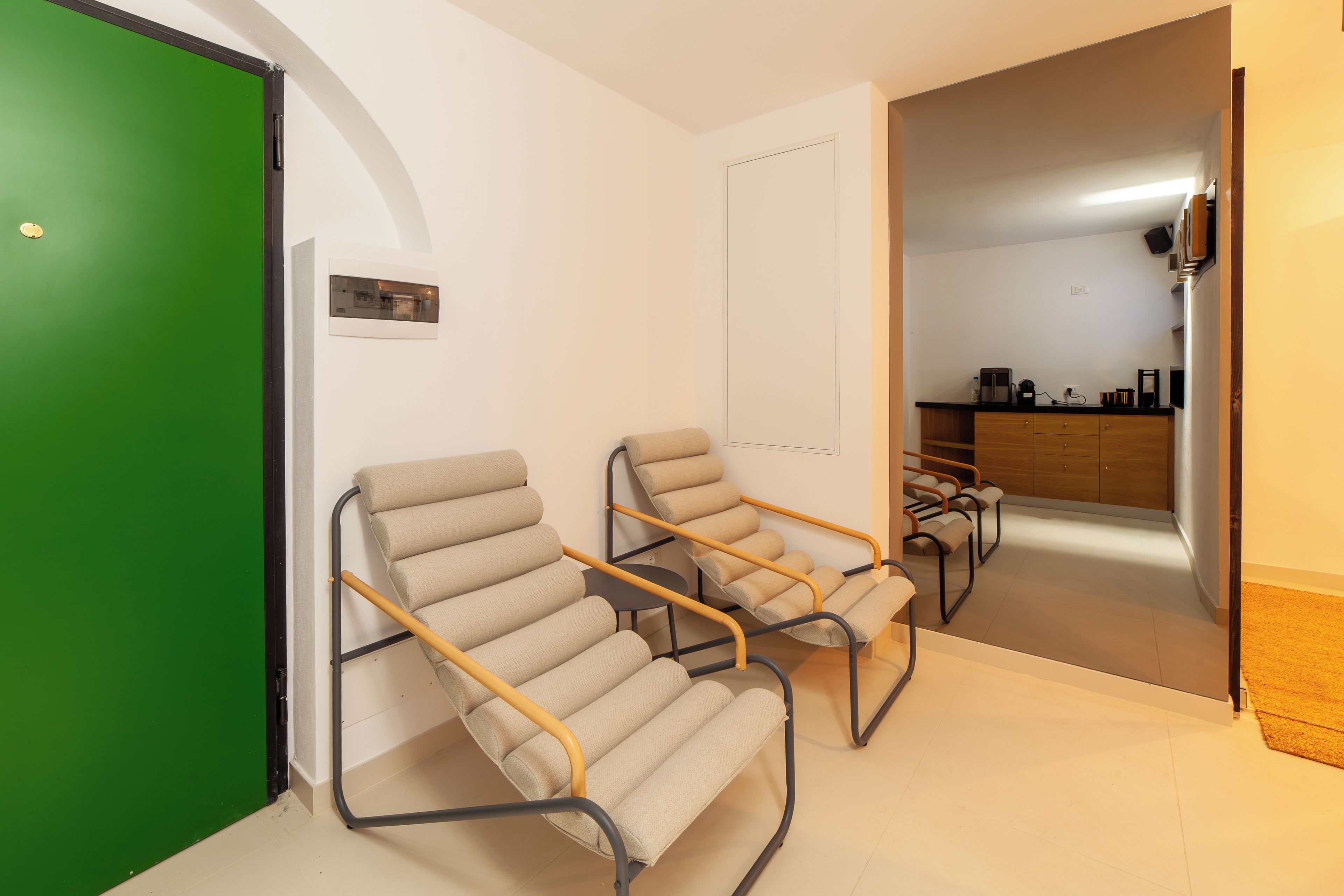 A room with two reclining chairs, a green door, and a kitchen area in the background.