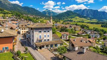 A town with a prominent building featuring a tower, surrounded by residential houses and lush green hills.