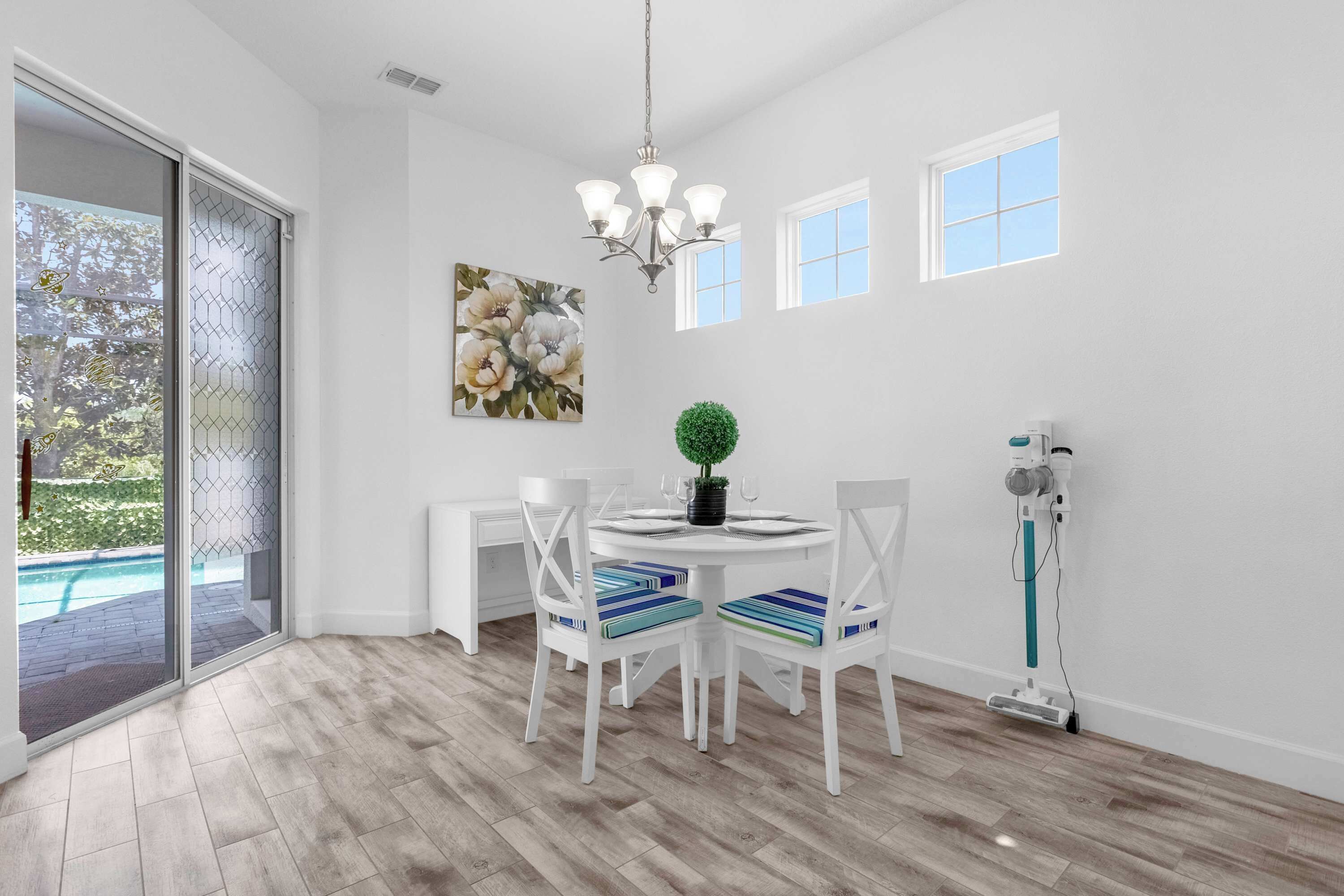 A dining area with a round table, white chairs, a chandelier, and a painting on the wall.