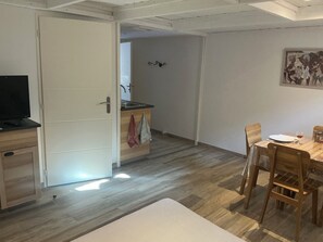 Une pièce comprenant une table à manger en bois, des chaises, un téléviseur et un coin cuisine avec un évier et des placards.