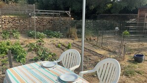 Uma área de refeições ao ar livre com uma mesa posta para dois, cercada por um muro de pedra e uma cerca.