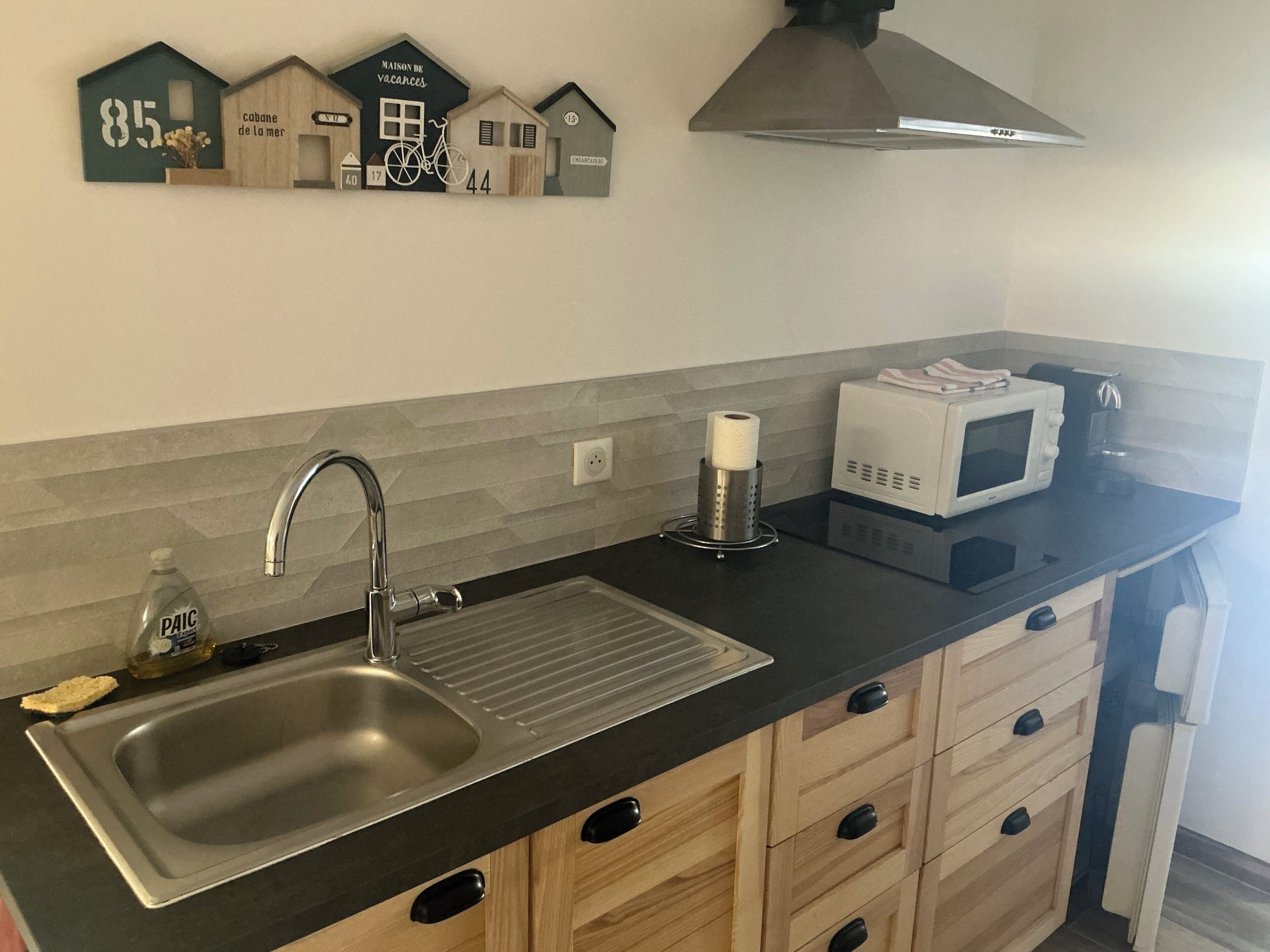 Uma cozinha com uma pia de aço inoxidável, micro-ondas, rolo de papel toalha e um objeto decorativo na parede com números de casa e uma bicicleta.