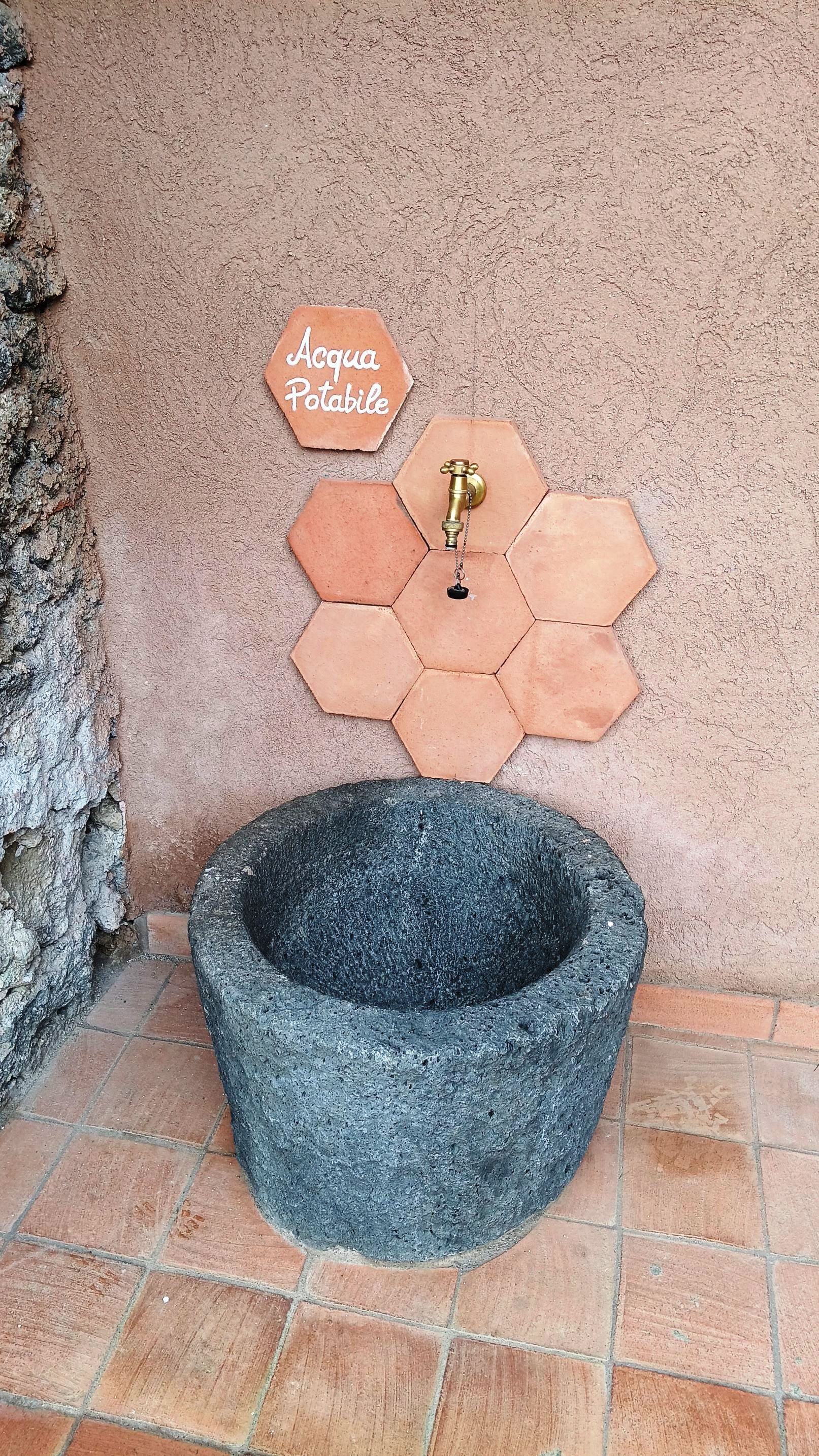 Ein Steinschale mit einer sechseckigen Fliesenwand und einem Schild mit der Aufschrift 'Acqua Potabile'.