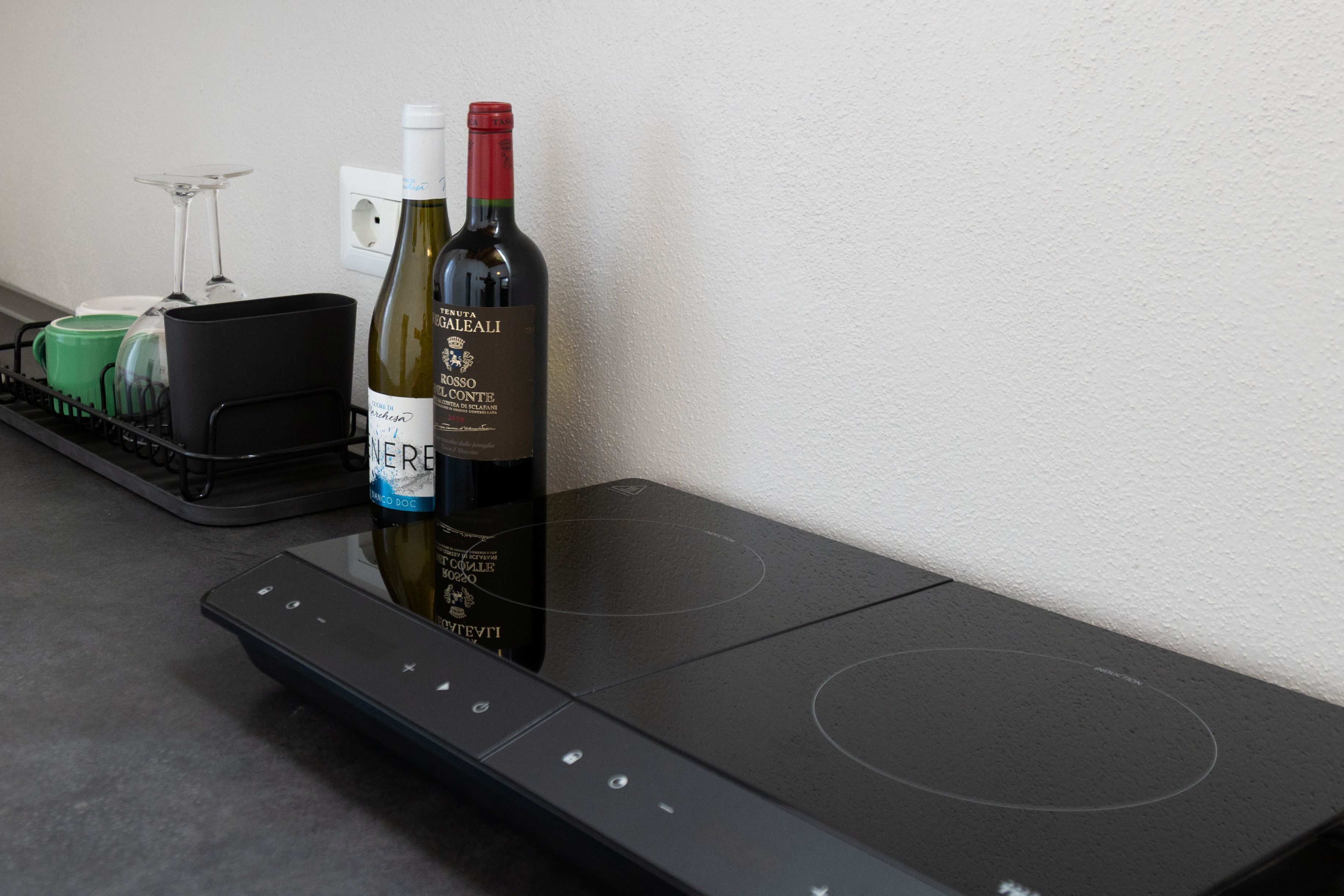 A kitchen with a black induction cooktop, a wine bottle, and a wine glass on the counter.