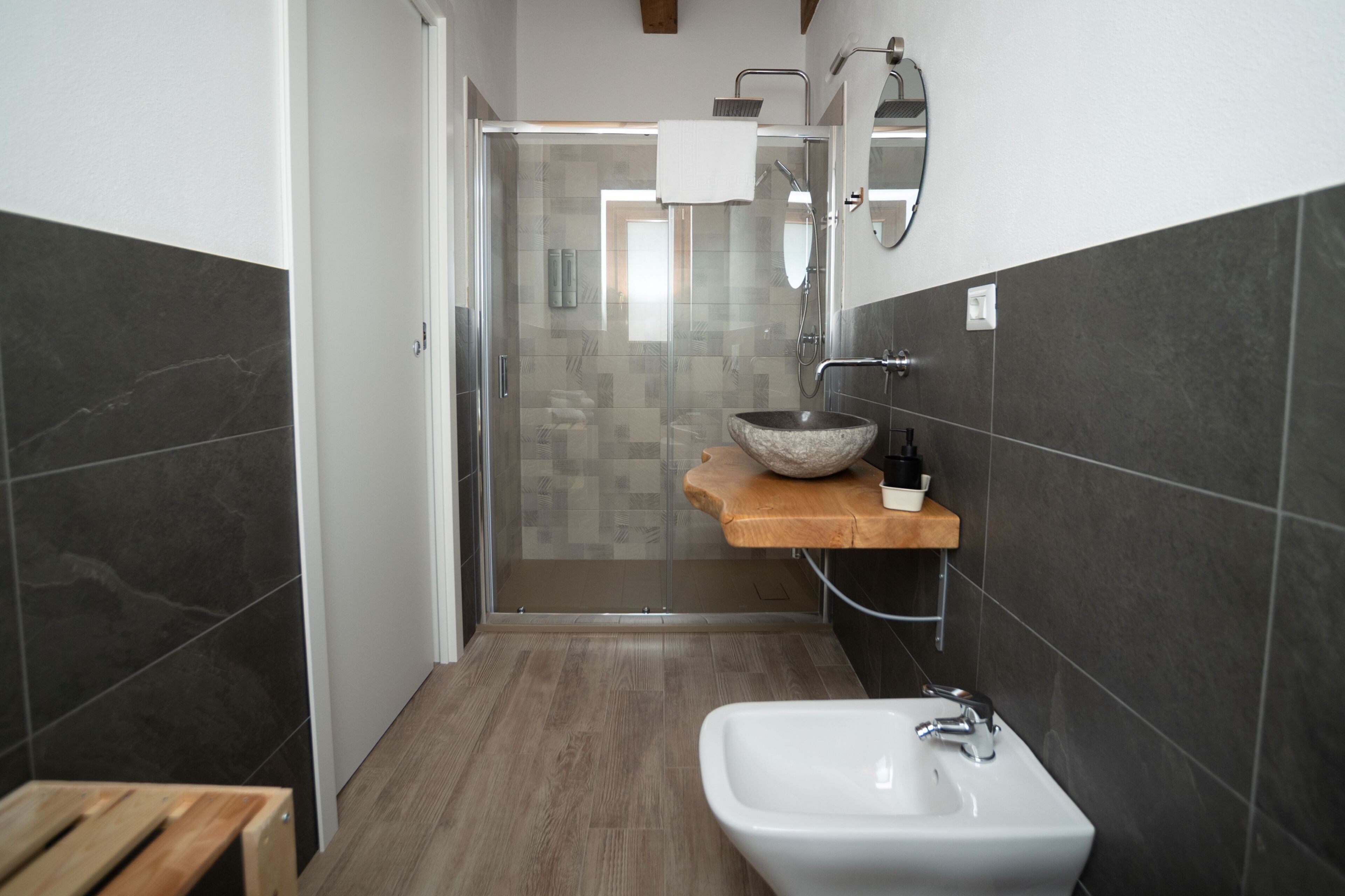 Un baño moderno con cabina de ducha de vidrio, tocador de madera y lavamanos blanco.