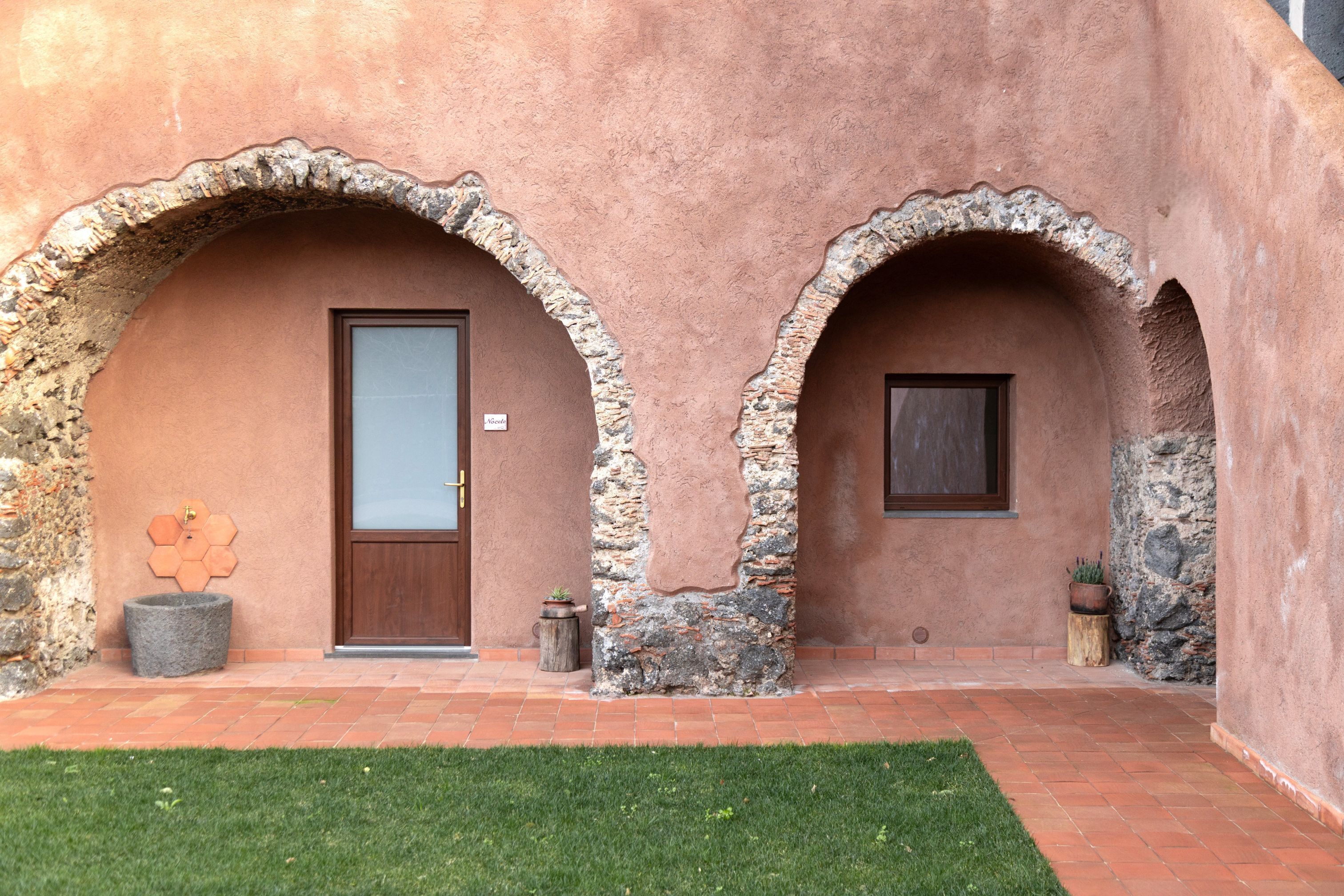 A building with two arched doorways, a stone wall, and a small garden area.