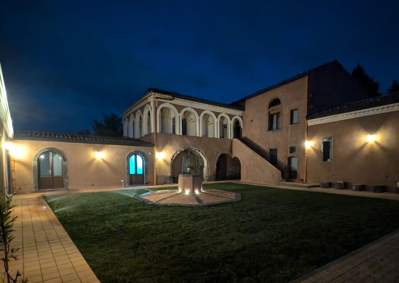 A courtyard with a fountain, arched doorways, and a building with a tiled roof.