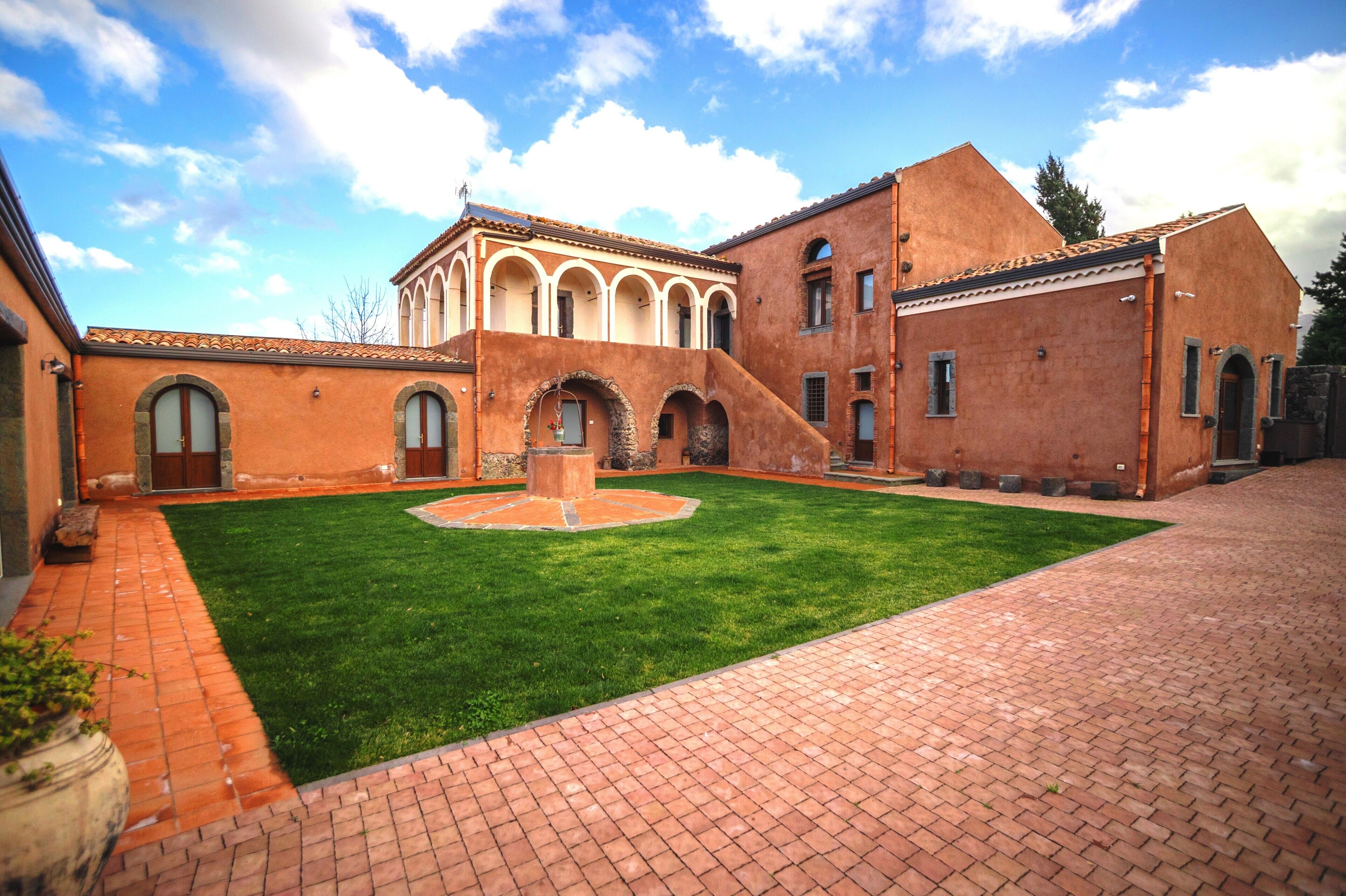 A courtyard with a central fountain, brick pathways, and a building with arched windows and a tiled roof.