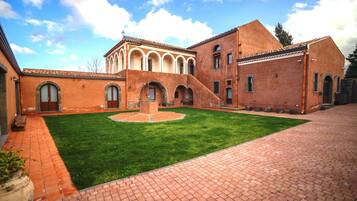 A courtyard with a central fountain, brick pathways, and a building with arched windows and a tiled roof.