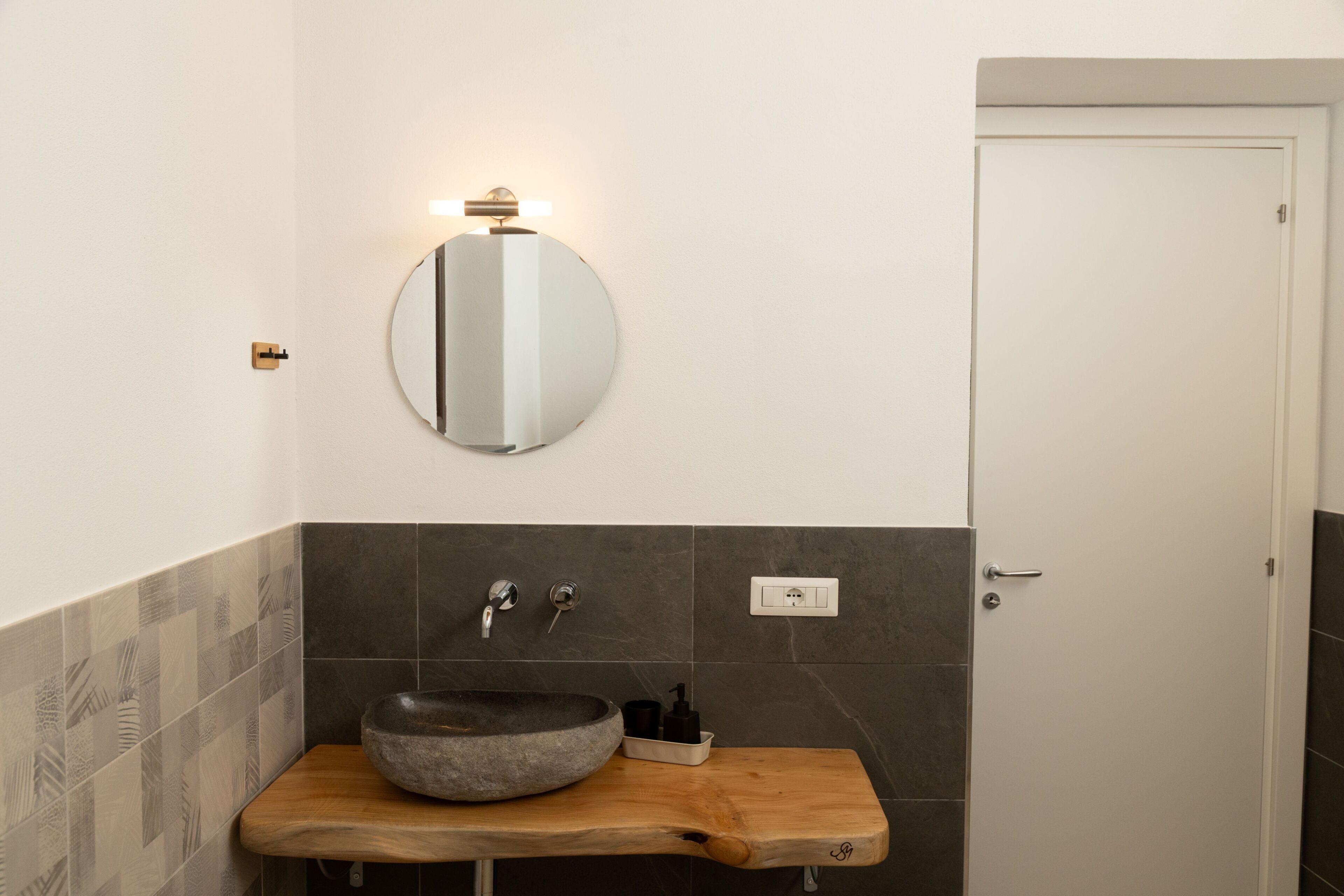 A bathroom with a round mirror, a stone basin, and a wooden countertop.