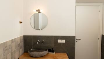 A bathroom with a round mirror, a stone basin, and a wooden countertop.