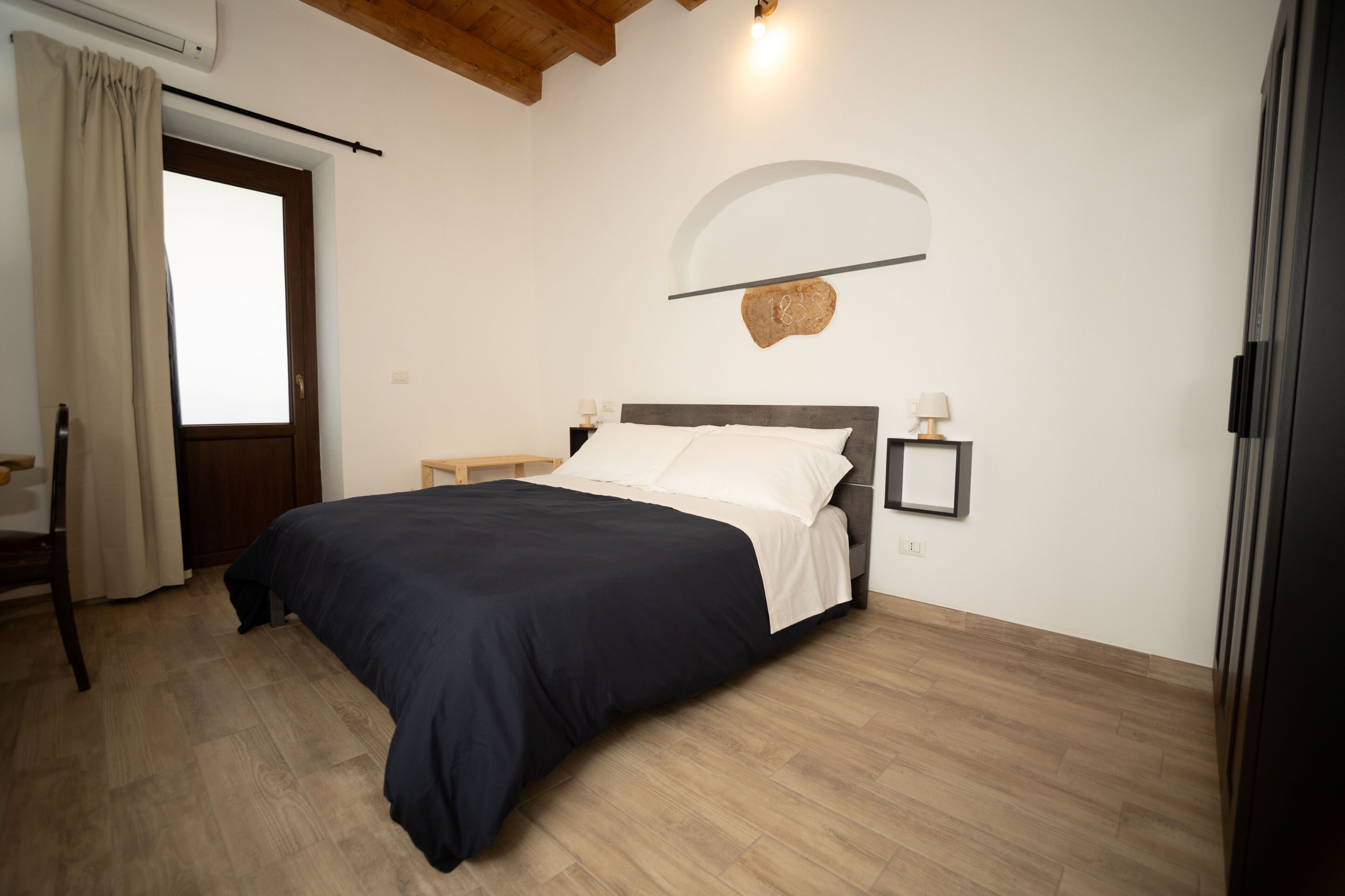 Un dormitorio con cama, mesita de noche, lámpara de pared y puerta con cortinas.