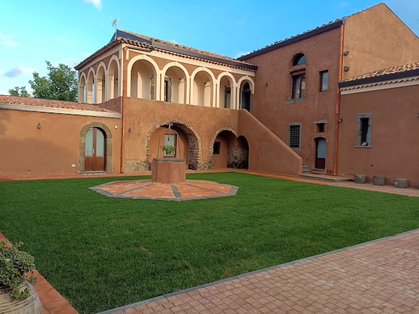 Un patio con una fuente central, un edificio con arcos y un césped bien cuidado.