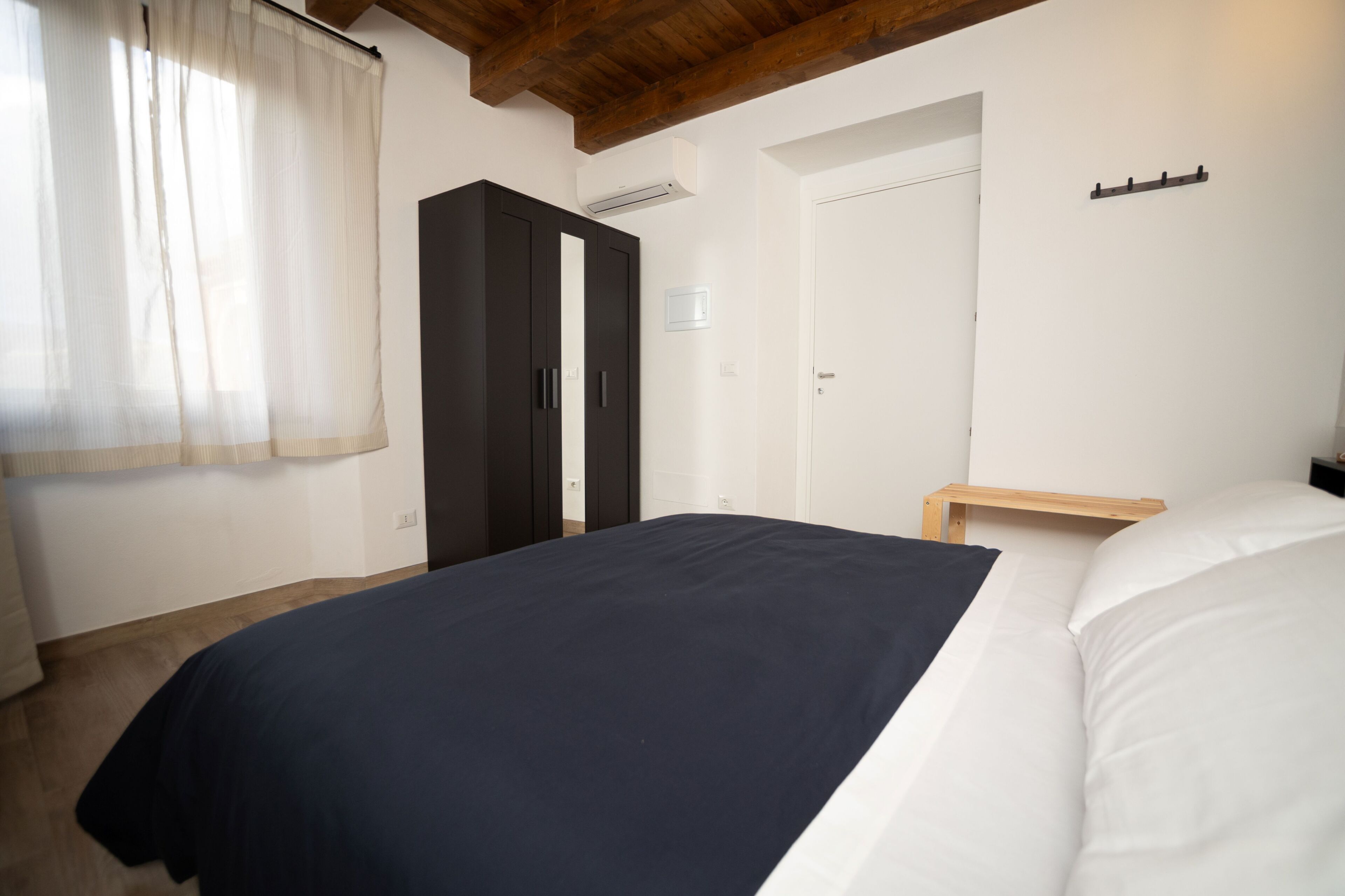 Een slaapkamer met een bed, een kledingkast, een nachtkastje en een raam met gordijnen.