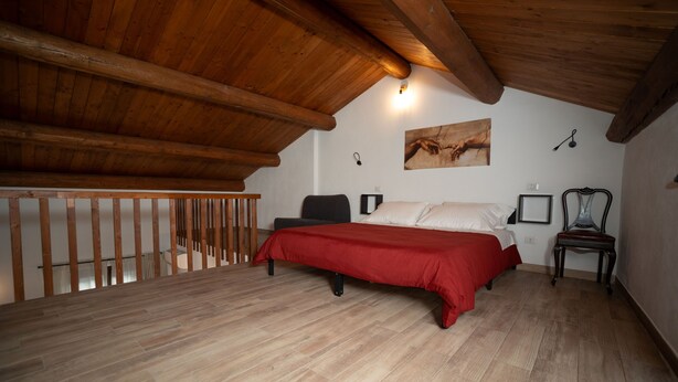 Un dormitorio con techo de madera, una cama con colcha roja, una silla y un cuadro en la pared.