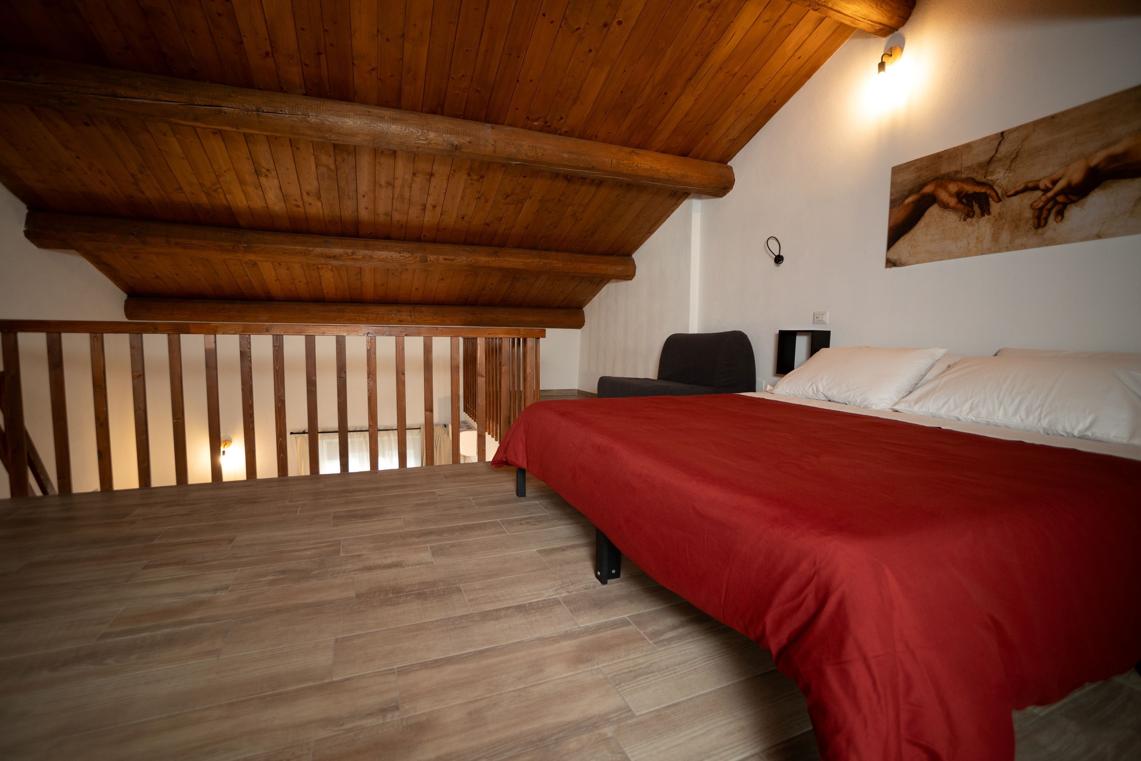 Ein Schlafzimmer mit Holzboden, einem Bett mit roter Bettdecke und einem Gemälde an der Wand.