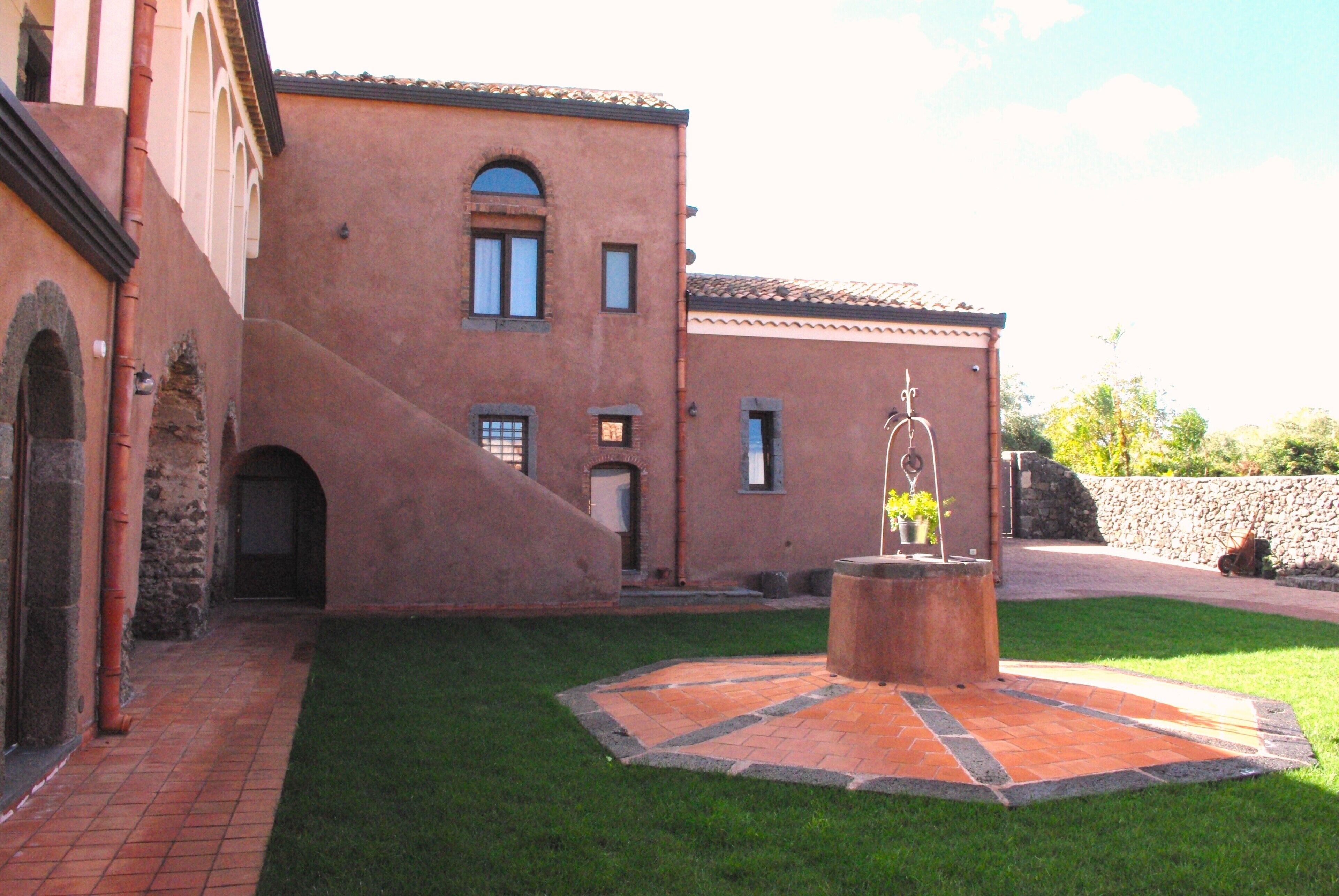 Un patio con una fuente, un sendero de ladrillos y un edificio con ventanas de arco y techo de tejas.