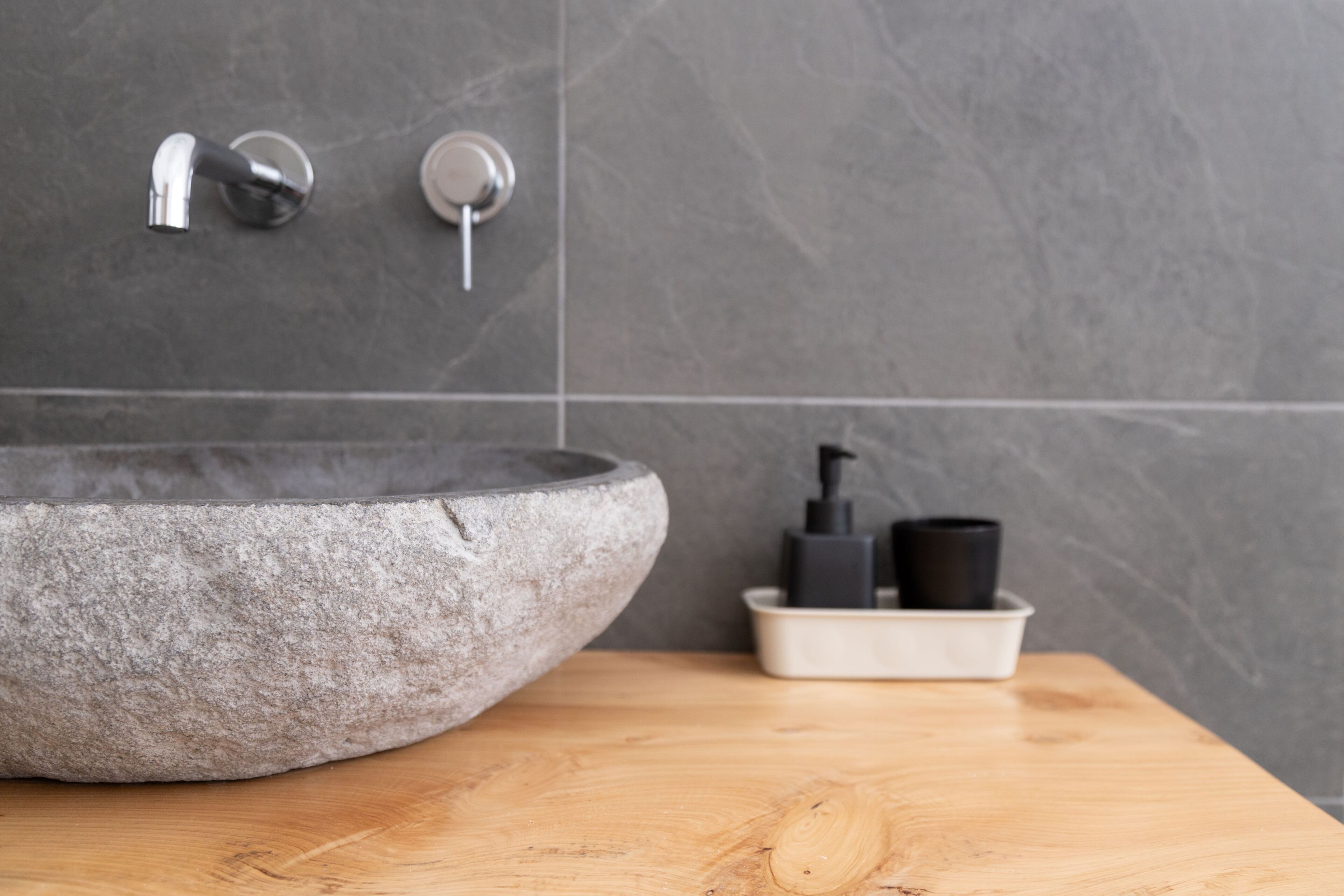 A bathroom with a stone sink, a faucet, and a soap dispenser on a wooden countertop.