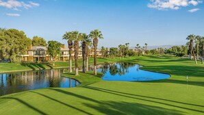 Un campo de golf con un estanque, palmeras y un club de campo.