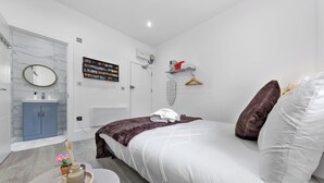Un dormitorio moderno con cama, mesita de noche con bandeja, espejo, armario, televisor de pared y estante con toallas.